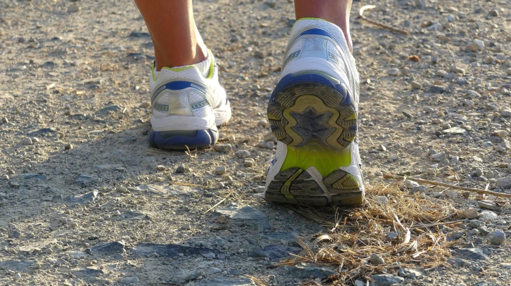Primer plano por detrás de zapatillas cómodas de correr blancas con detalles azules en un camino de tierra y grava.