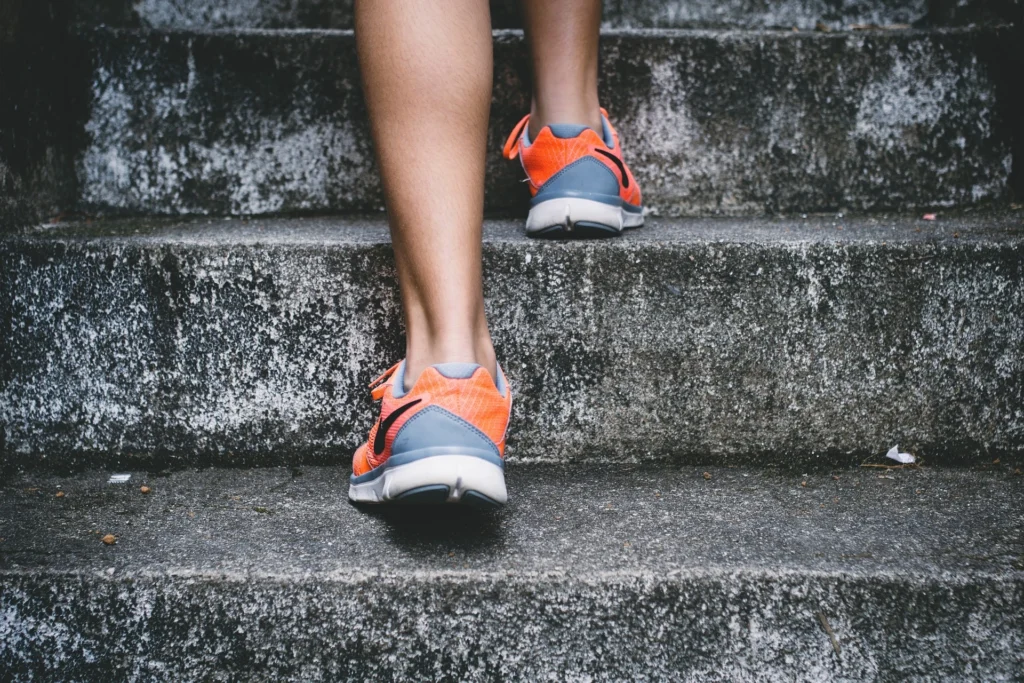 Primer plano de zapatillas cómodas de running naranjas subiendo escaleras de hormigón de textura irregular.