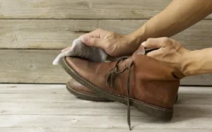 Persona limpiando con un paño húmedo unas botas de piel marrón, un cuidado esencial para mantener la flexibilidad de tus zapatos comodos.