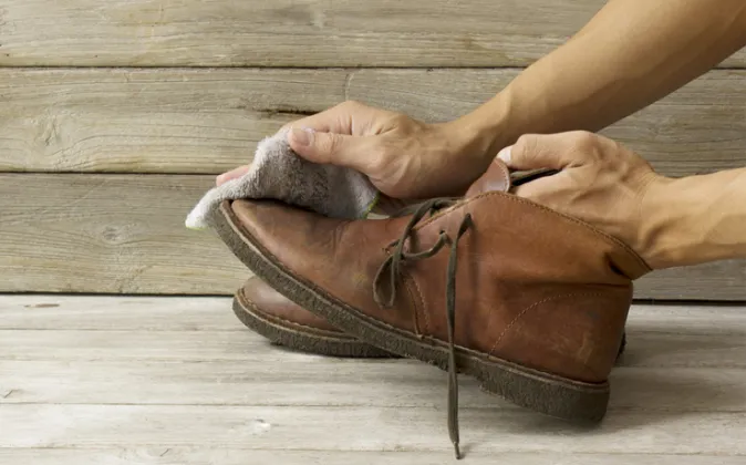 Persona limpiando con un paño húmedo unas botas de piel marrón, un cuidado esencial para mantener la flexibilidad de tus zapatos comodos.