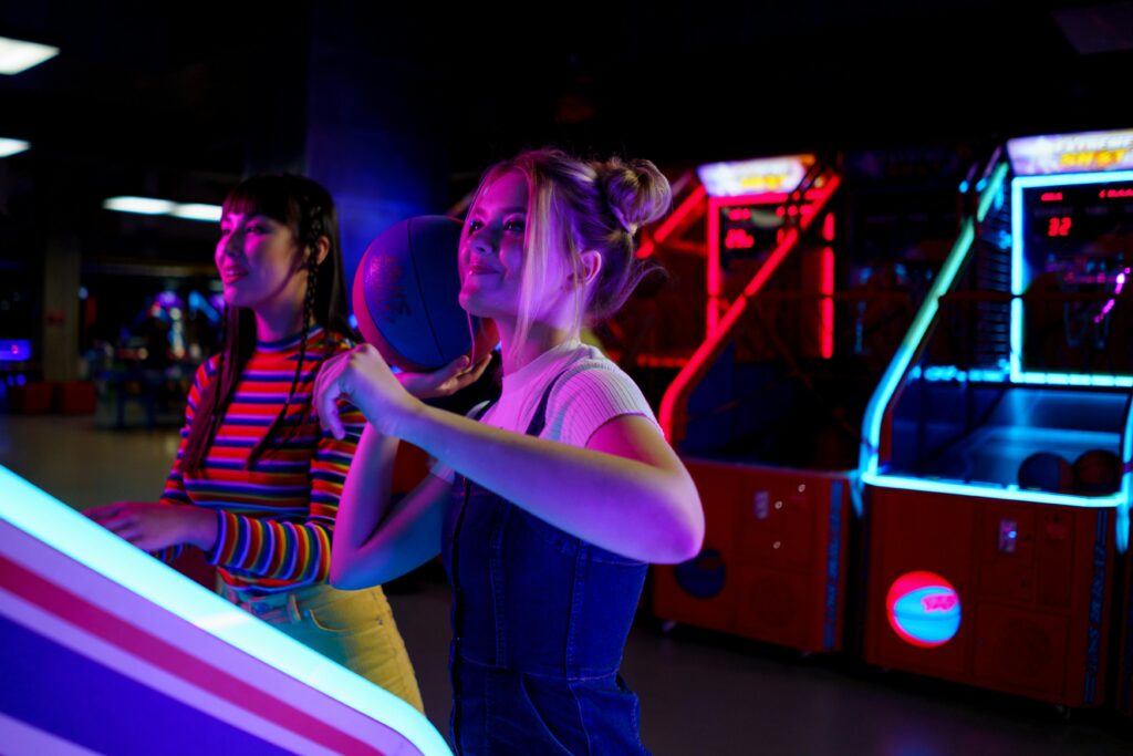 imagen aproximada de personas jugando en la máquinas recreativas de baloncesto decoradas con luces neones.